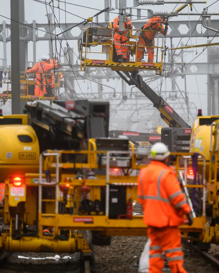 Network Rail engineers in orange PPE working on overhead line equipment beside the track